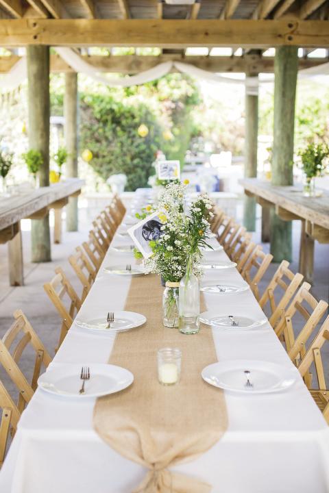 FÊte Set: Reception tables from Snyder Event  Rentals were kept simple with a burlap runner and a rustic arrangement of flowers. For table numbers, the couple printed numerals on photos of their dogs and tucked them into the flower arrangements.