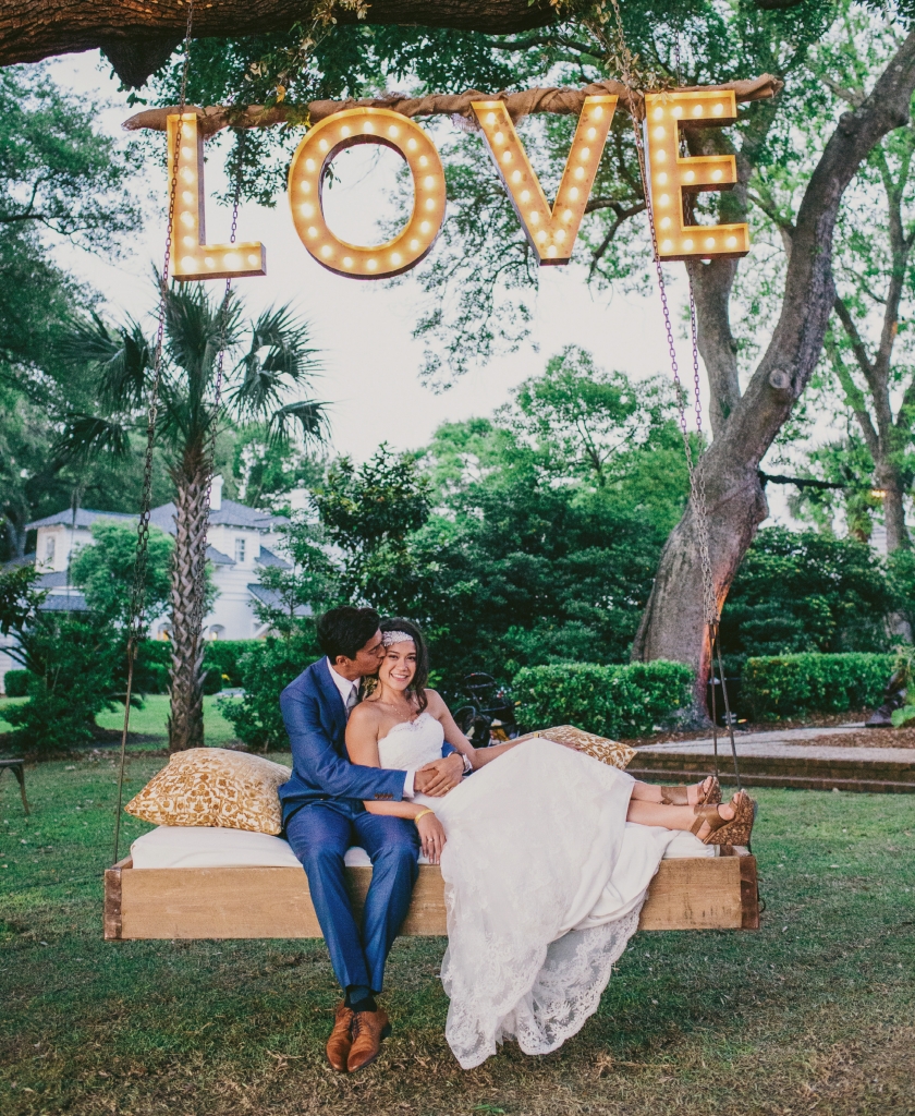 Photograph by Hyer Images at Lowndes Grove Plantation. Swing by Ooh! Events. Love sign by Loluma. Bride&#039;s attire by Marchesa (gown); Doloris Petunia (hair accessory).