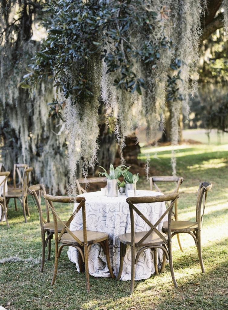 “I am definitely a ‘no frills’ girl and John is a Southern outdoorsman  in the truest form,” says bride Hollis, who worked with designer Calder Clark to  pick a palette lifted from the Lowcountry landscape. Here, gray paisley linens  dressed tablescapes topped with greens.  Tables and chairs by Snyder Events. Linens by La Tavola. Florals by Blossoms Events. Photograph by Tec Petaja.