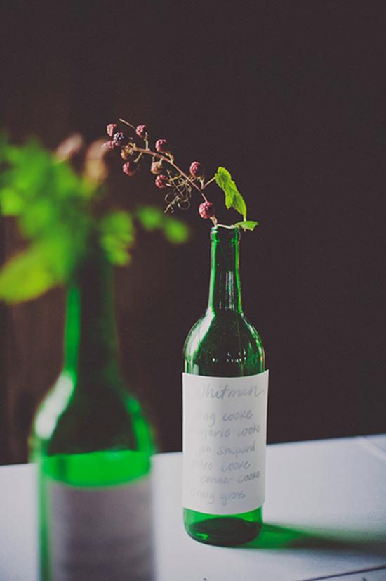 MESSAGE ON A BOTTLE: Green wine bottles, topped with raspberry branches and adorned with handwritten quotes from the couple’s favorite authors, served as table numbers.
