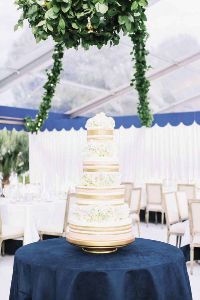 Perched atop a table covered in the same sueded navy fabric that trimmed the other linens, the dessert from Wedding Cakes by Jim Smeal wore fondant ribbons of gold and pink.