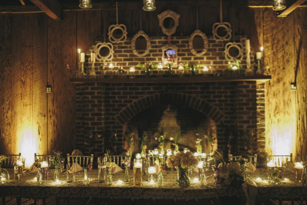 SIMPLE TOUCHES: The location’s rustic beauty was aglow with myriad candles. The hearth was filled with a gentry of tall flowers, while white-framed mirrors hung above the mantel.