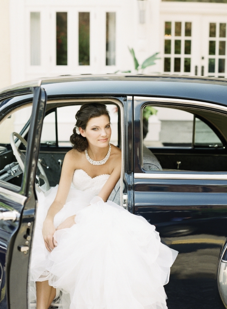 Pronovias’ “Beca” mermaid-style gown with embroidered sweetheart bodice and tulle and organza ruffled skirt from Gown Boutique of Charleston. Crystal hair clip from Jean’s Bridal. Mariell’s rhinestone  collar necklace from White on Daniel Island. 1950 Chevrolet Bel Air Deluxe car from Lowcountry Valet &amp; Shuttle Co. Image by Corbin Gurkin, photographed at The Vendue.