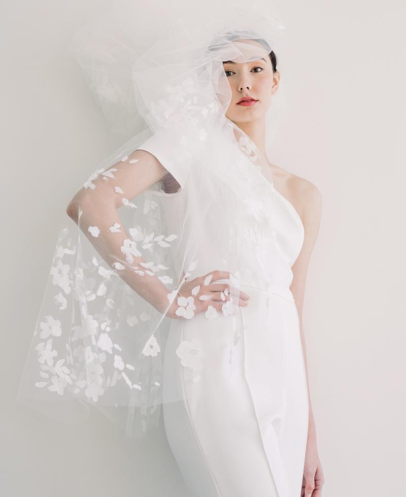 Amsale Nouvelle’s one-shoulder crepe jumpsuit from Maddison Row South. Katherine McDonald’s “Riverland” hand-painted veil (shown gathered) from Kate McDonald Bridal