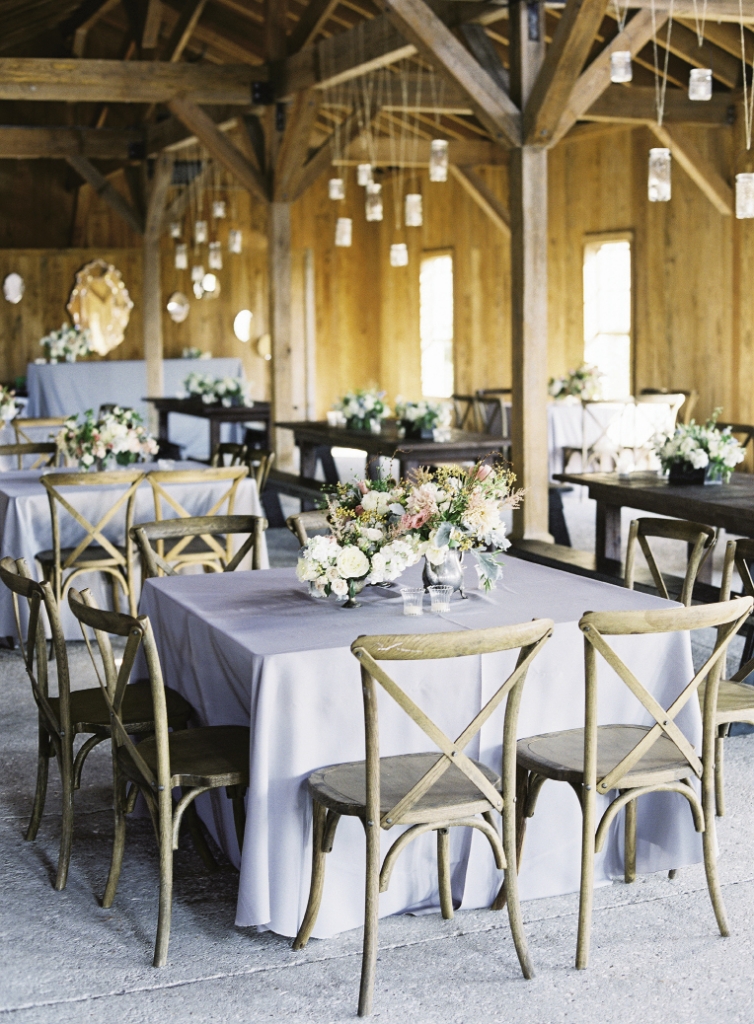 WOODWORKS: Silver-gray linens and pale, unfinished wooden chairs from Snyder Events kept the reception room light overall, while Snyder’s dark-stained farm tables added depth to the design. “Marianna wanted a look that felt like things had been collected from someone’s own home,” Heather says of the bride’s aesthetic. A mix of vessels from Heather’s collection—including an antique pewter teapot—and varying floral  arrangements did just  the trick.