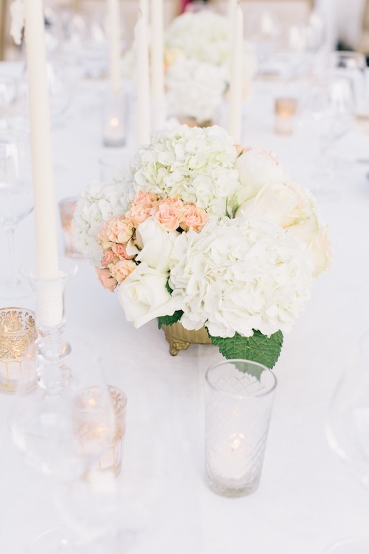 Harkening colors from invitation suite and the hand-held bouquets, arrangements of leafy white hydrangeas, white roses, and pale pink spray roses dotted the dining tables.