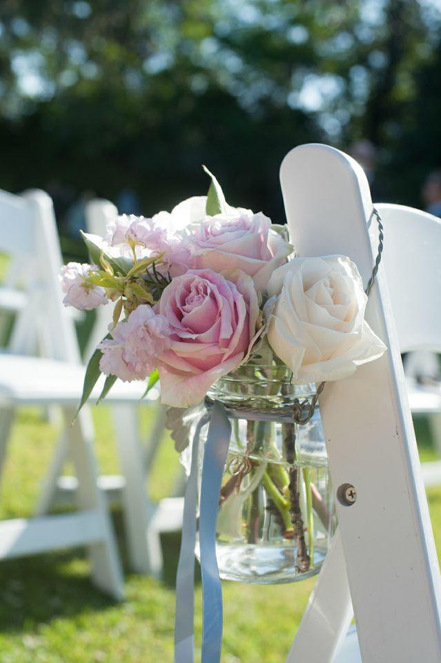 PINK ‘N’ BLUE: Blue ribbon-tied Mason jars filled with light pink roses, white roses, and carnations hung from chairs that lined the aisle.