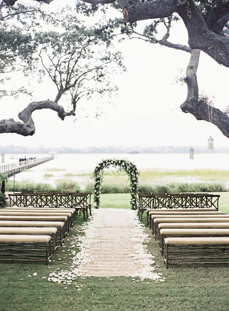 Easton Events dressed the ceremony in their hallmark elegant style, with an arbor of softly draping greens and fragrant white blooms by Sara York Grimshaw Designs; a seagrass runner edged with fresh rose petals; and benches bearing natural-hued linen cushions from Snyder Event Rentals.