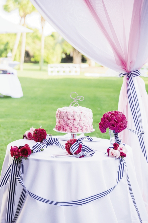 SO SWEET: Dressing the cake table with bridesmaid bouquets is a traditional idea, but how about using flower girl kissing balls and posies, too? Here, a pink ombré treat from Ashley Bakery gets just that treatment. To play up the palette further, ribbon was draped as swag and used as curtain tie-backs. “I loved the feminine pink combined with the crisp navy and white stripe,” says Ashley.