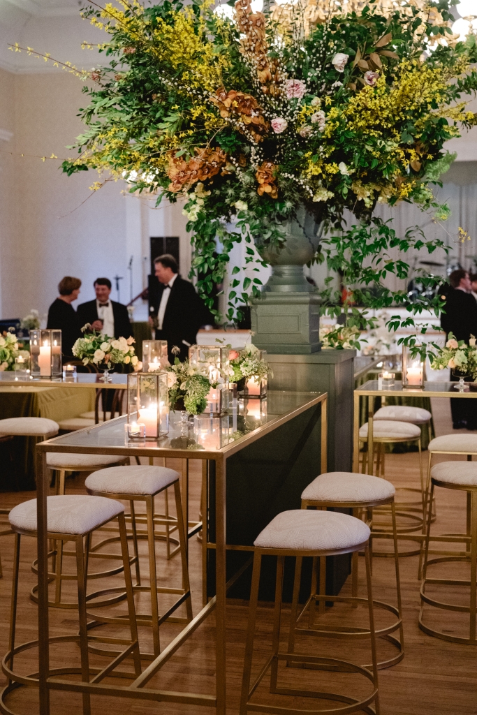 “Moody yet bright” was among the minimal design direction Libby gave the team at Gathering Events, which they delivered through dramatic branching displays of forsythia and greenery, sumptuous fabrics, and collections of glass hurricanes and votives.