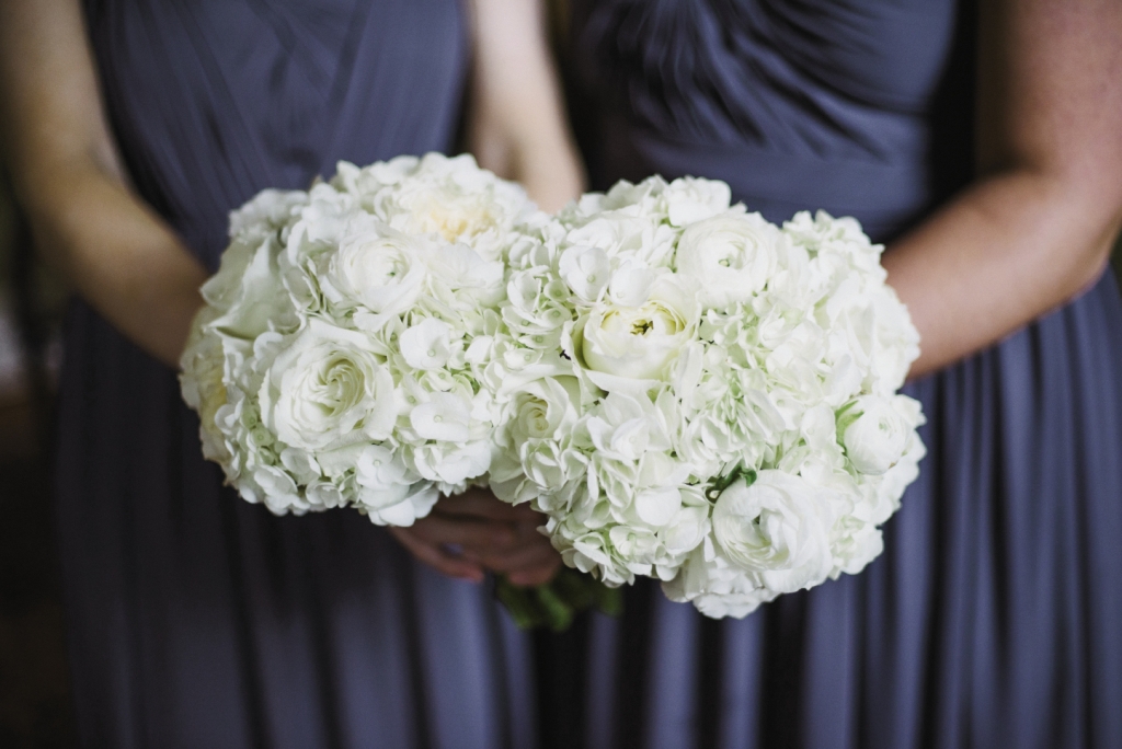 IN HAND: All-white bouquets of hydrangeas, garden roses, and ranunculus by Gayla Harvey of Tiger Lily Weddings offset the bridesmaids’ navy dresses.