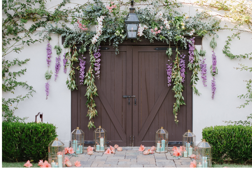 The ceremony took place with the property’s carriage house as a backdrop. To complement existing vines on the building, Anne Bowen Dabney of Charleston Stems crafted an arbor-like array of orchid sprays, tulip bundles, and eucalyptus branches, then hung hybrid delphinium and eucalyptus garlands from it. Amaryllis blooms were artfully scattered amid lanterns with celadon green candles. (Image by Natalie Franke Photography)