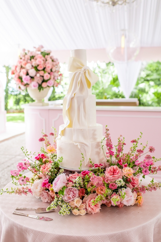 A jubilant ring of roses, peonies, hibiscuses, and chamomile flowers encircled the sculptured cake.