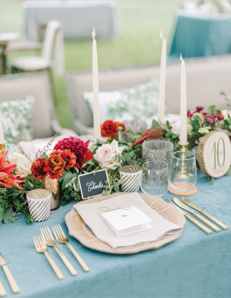 More formal décor elements like gold mercury hurricane candleholders, gleaming cutlery, and stately taper candles are offset by laid-back accents of feathered votives and hand-painted wooden slabs, creating a design that is both rustic and refined.