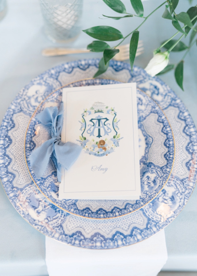 Memorable Menus - An illustrated wedding crest can grace everything from invites and signage to cups and koozies. Here, it adds a touch of whimsy to elegant place settings in a shared color palette.