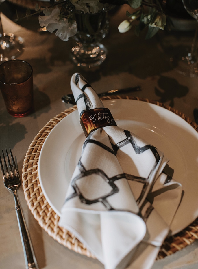 The décor featured rattan, checkered marble, greenery, stoneware, pewter, candles, and personalized tortoiseshell napkin rings.