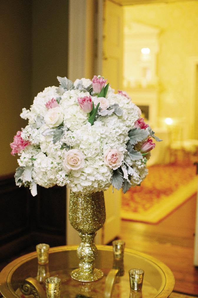 Think big (and gold) for entrance décor. Here, glitter completely covers a chalice topped with an arrangement of hydrangeas, fringe tulips, garden roses, hypericum berries, ranunculus, and sweet peas in cream, blush, and caramel colors by Whitney Randall of Branch Design Studio.